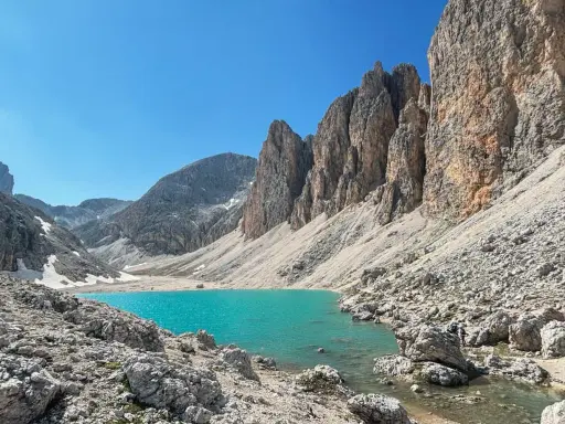 Il **lago di Antermoia**, incastonato tra imponenti pareti rocciose, brilla di un turchese intenso sotto un cielo azzurro.