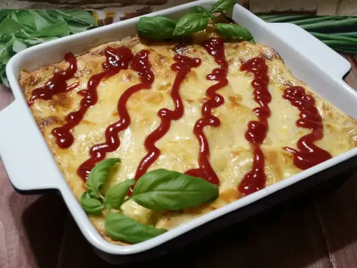Pyszne, zapieczone fit lasagne w białym naczyniu, polane ketchupem i ozdobione listkami bazylii.