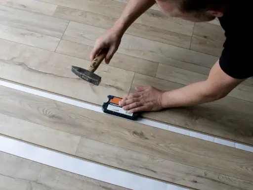 Mann verlegt Laminat mit Hammer und Schlagklotz. Die neuen Dielen werden präzise zusammengefügt.