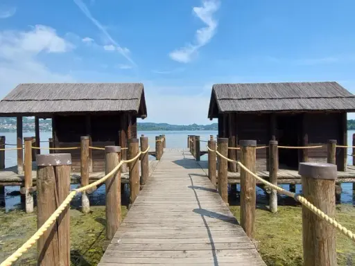 Pontile in legno con due capanne sul lago di Viverone, sotto un cielo azzurro con nuvole bianche.