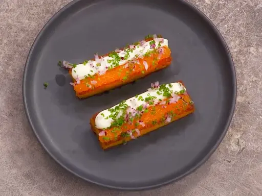 Två gyllene, rektangulära tater tots toppas med gräddfil, finhackad rödlök och gräslök.