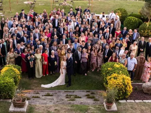 Una gran familia celebra una boda íntima al aire libre. Todos posan sonrientes para la foto grupal en un jardín verde.