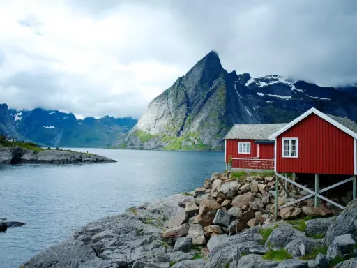 Två röda stugor vid en sjö med dramatiska berg i bakgrunden. Perfekt för att vandra i Norge.
