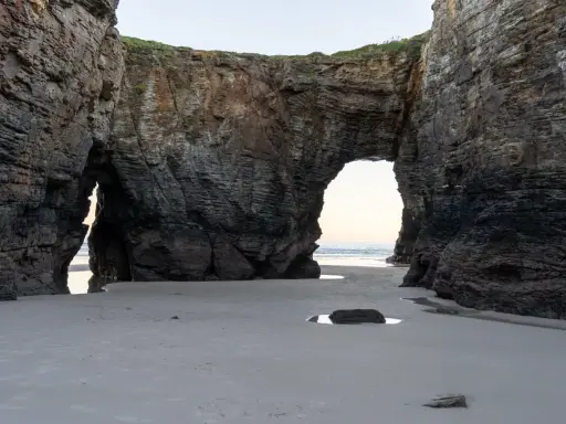 Felsbögen am Praia das Catedrais, die wie Kathedralen wirken, mit Sand und Meer im Hintergrund.