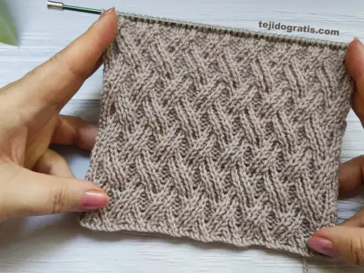 Manos sostienen un tejido cruzado de lana beige con un patrón de rombos entrelazados.