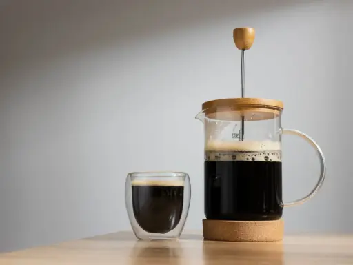 Frisch gebrühter Kaffee mit Wasser in einer French Press und einem Glas. Der Duft von Kaffee liegt in der Luft.