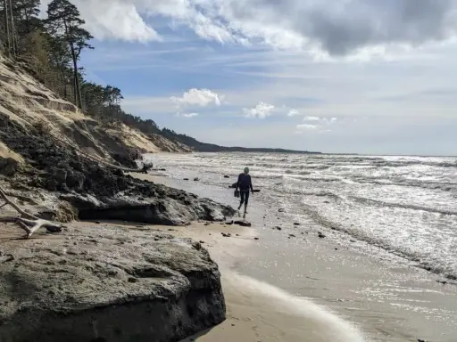 Spacerująca osoba na plaży w Ustce, w oddali widać orzechowo-brązowe klify.