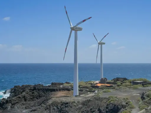 Zwei Windräder an einer felsigen Küste Spaniens, die saubere Energie erzeugen.