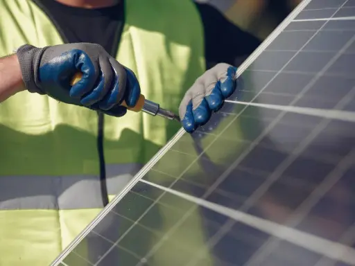 Mains nues, gants bleus et jaunes, tournevis en action pour la réparation d'un panneau solaire.