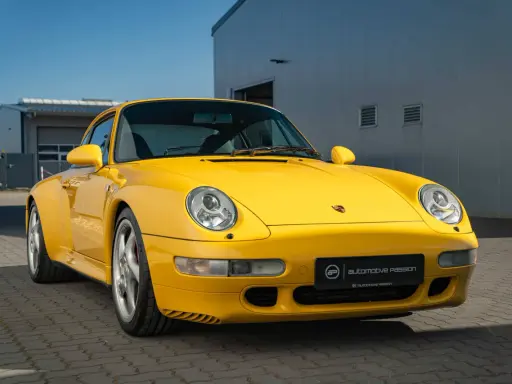 Gelber Porsche 993 vor einem modernen Gebäude. Die Wertentwicklung dieses Klassikers ist bemerkenswert.
