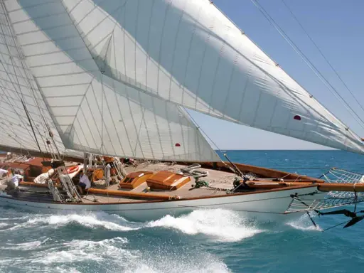 Eine elegante 12mr Yacht gleitet über das türkisfarbene Meer, die weißen Segel strahlen in der Sonne.