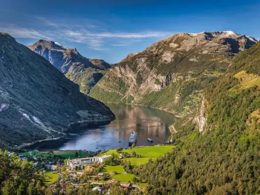 Majestätische norwegen fjorde mit einem Kreuzfahrtschiff, das auf dem ruhigen Wasser fährt. Grüne Berghänge und ein kleines Dorf am Ufer.