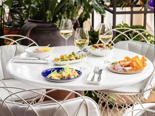 Delicioso brunch con niños en Madrid. Mesa con varios platos, copas de vino blanco y sillas blancas.