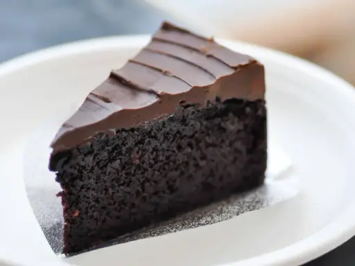 Una fetta di torta al cioccolato senza burro, soffice e ricoperta da glassa al cioccolato, servita su un piatto bianco.