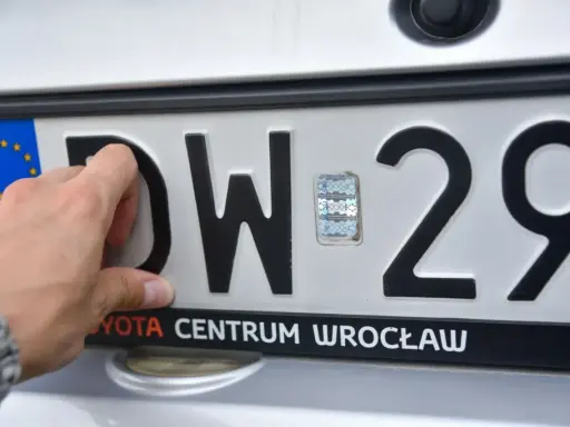 Dłoń dotyka polskiej tablicy rejestracyjnej z literami DW i cyframi 29.