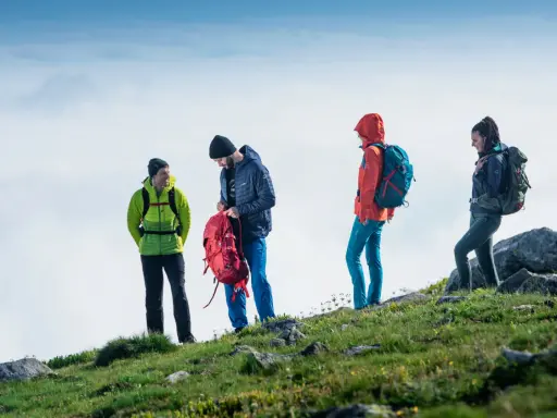 Cztery osoby w kolorowych kurtkach i plecakach na tle nieba. To właśnie **outdoor**, czyli aktywność na świeżym powietrzu.