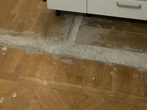Arbete pågår för att ta bort laminatgolv. Ett vitt pulver och grått material syns på det gamla trägolvet.