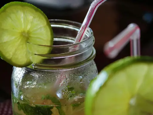 Orzeźwiający mohito drink, z widocznymi składnikami: limonką i miętą, w szklanym słoiku z rurką.