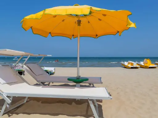 Lettini e ombrelloni gialli sui bagni Rimini, con pedalò gialli pronti per il mare azzurro.