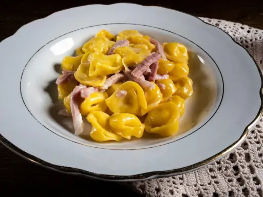 Tortelli ripieni in salsa cremosa con prosciutto, un classico tra i piatti tipici di Parma, serviti in un piatto bianco bordato d'oro.