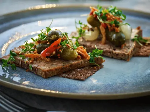 Två bitar mörkt bröd med leverpastej, toppade med cornichoner, chili och krispiga topping. Ett enkelt leverpastej recept att inspireras av.