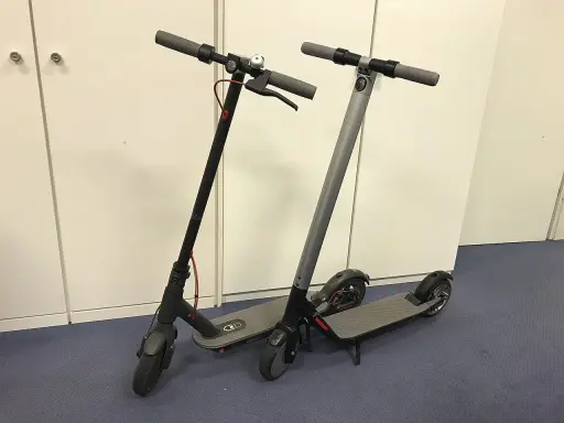 Deux trottinettes électriques, noires et grises, prêtes à l'emploi. La trottinette électrique définition : un moyen de transport urbain pratique.