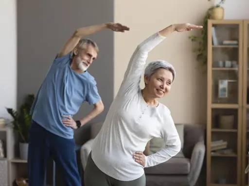 Uśmiechnięta para seniorów ćwiczy w domu. Aktywne zajęcia dla seniorów to świetny sposób na zdrowie i dobre samopoczucie.