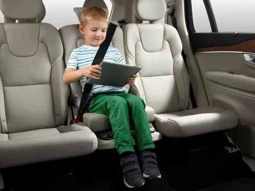 Niño en asiento elevador integrado, con cinturón de seguridad puesto, usando una tablet. ¿Cuál es el asiento más seguro del coche?