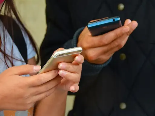 Zwei Hände halten Smartphones. Eine Frau hält ein goldenes iPhone, ein Mann ein blaues Handy. Vielleicht kommen eingehende Anrufe nicht an.
