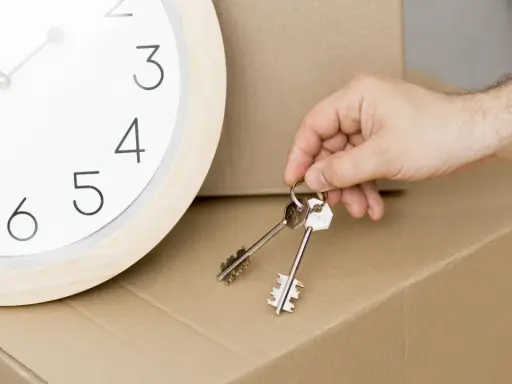 Un reloj marca el tiempo mientras una mano sostiene las llaves, simbolizando la inminencia de un contrato de alquiler temporal y una mudanza.