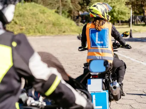 Rozpoczyna się kurs na motocykl. Uczestnicy w kamizelkach z literą "L" ćwiczą jazdę na placu manewrowym.