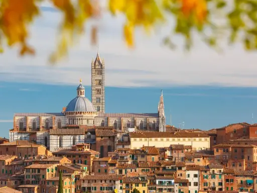 Vue panoramique de la ville de Sienne, avec sa cathédrale imposante et ses toits de tuiles ocres, baignée par la lumière dorée de la terre de sienne.