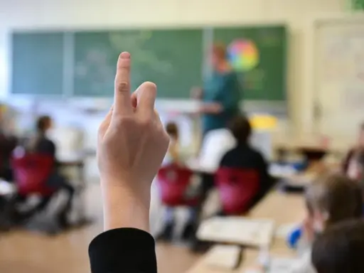 Ein Finger zeigt nach oben im Klassenzimmer. Dies symbolisiert die **Schulpflicht in Deutschland**, wo Kinder lernen und Fragen stellen.