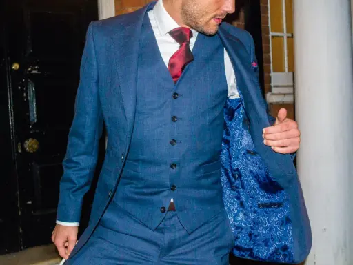 A man in a blue checkered suit, white shirt, and red tie. He's showing off the paisley lining of his jacket, and the bottom button on his vest is unbuttoned.