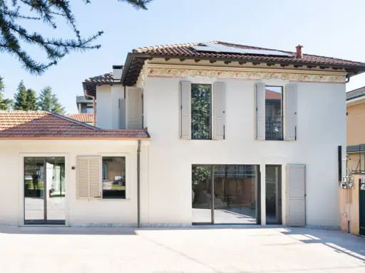 L'abbinamento colori facciata e serramenti crea un'armonia moderna. La casa bianca con dettagli decorativi si fonde con le persiane e gli infissi grigio chiaro.