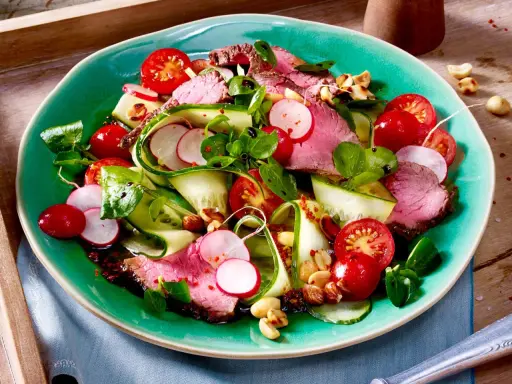 Saftiger Rinderbraten auf einem bunten low carb salat mit Gurke, Radieschen und Kirschtomaten. Nüsse sorgen für Crunch.