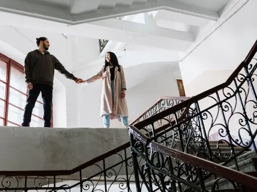 Pareja tomados de la mano en una escalera, ¿qué es ser posesivo? Él la mira, ella sonríe.