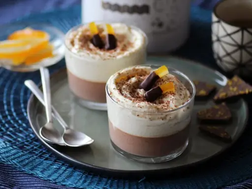Deux verrines 3 chocolat, garnies de crème fouettée, de copeaux de chocolat et d'écorces d'orange confites.