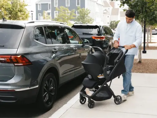Hombre empuja un cochecito con un sistema sujeción infantil silla coche, junto a un coche gris.