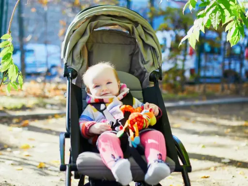 Uśmiechnięte dziecko w kolorowym sweterku siedzi w spacerówce, trzymając zabawkę.