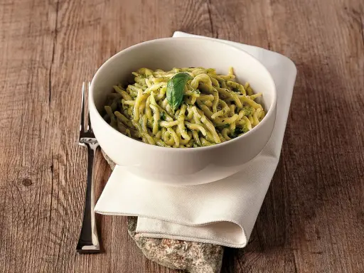 Un piatto invitante di trofie al pesto, guarnito con una foglia di basilico, su un tavolo di legno rustico.