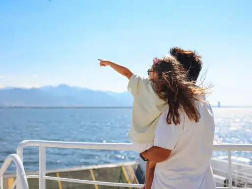 Bambina indica l'orizzonte da una nave, con la famiglia in vacanza a Favignana. Il mare azzurro e le montagne sullo sfondo creano un'atmosfera serena.