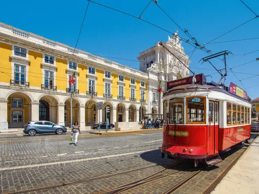 Röd spårvagn i Lissabon, perfekt för en resa med interrail europa. Gula byggnader och en solig dag.