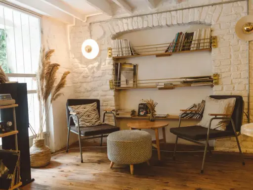 Acogedor rincón de lectura con sillas cómodas, mesa auxiliar, estanterías llenas de libros y plantas secas.
