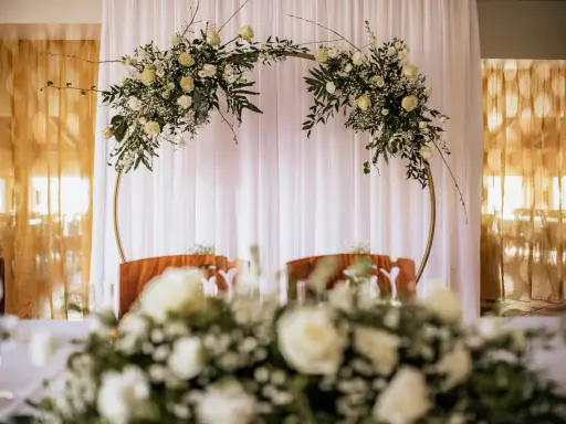 Elegancki ołtarz na ślub w plenerze, ozdobiony białymi kwiatami i zielenią na złotym okręgu.