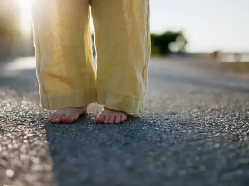Barfuß auf Asphalt, die weite Leinenhose im Abendlicht. Ein Gefühl von Freiheit, als ob die Hose frisch gewaschen wäre und bereit für neue Abenteuer.