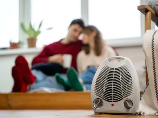 Pareja acurrucada con bebidas calientes, un radiador eléctrico en primer plano. Así funciona un radiador eléctrico para calentar el hogar.
