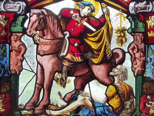 Święty Gracja na koniu przecina płaszcz dla żebraka. Witraż pełen symboli i postaci.