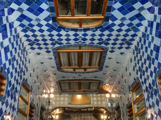 Interno della Casa Batlló: soffitto ondulato con piastrelle blu e bianche a rombi, finestre in legno e luci soffuse.