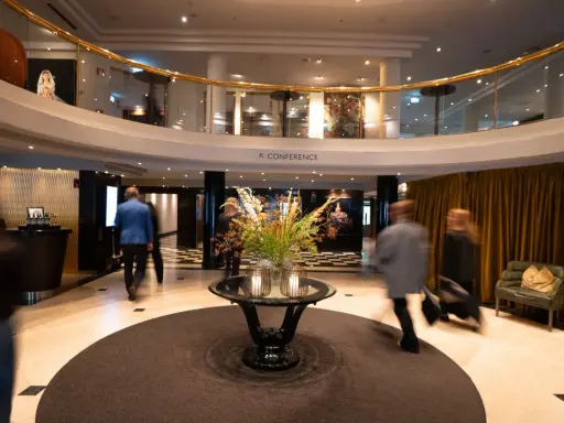 Elegant hotell park lobby med en blomsterdekor i mitten. Människor rör sig förbi i en suddig rörelse.